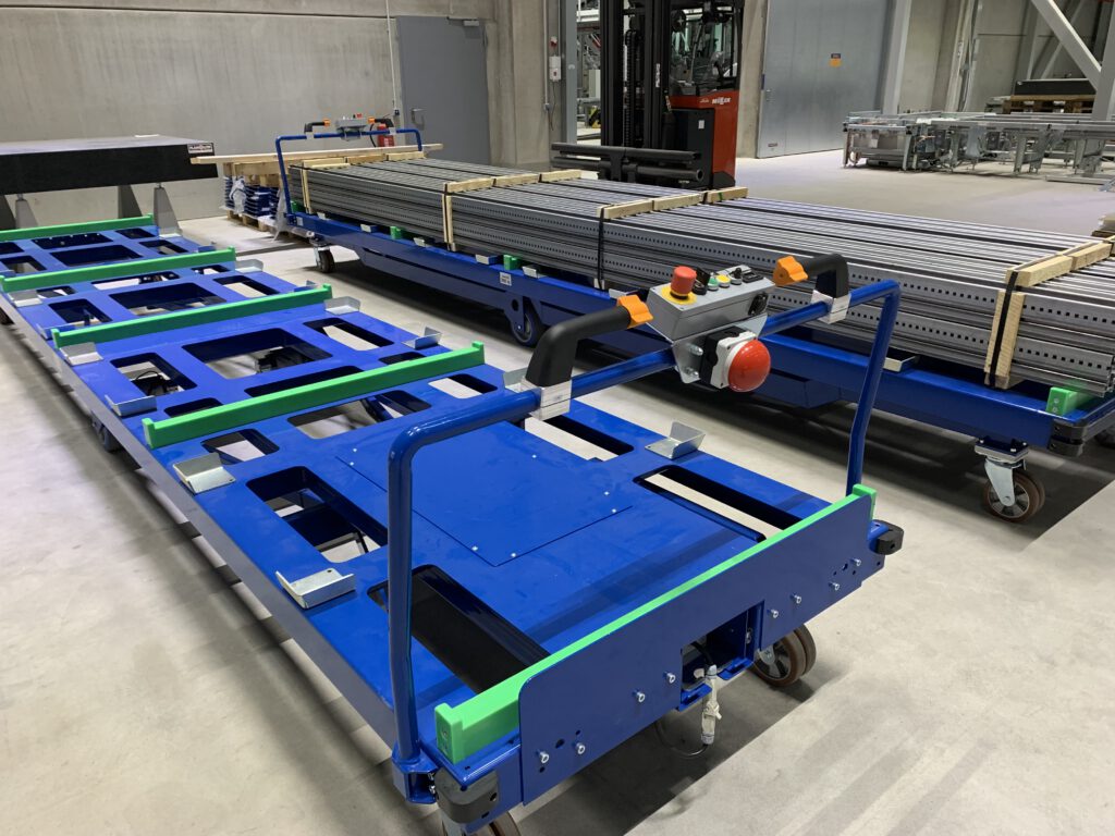 Blaue elektrisch angetriebene Langgutwagen mit Bedienpulten und grünen Auflagen in einer Industriehalle.