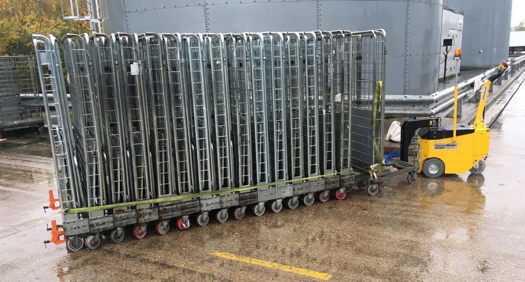 Gelber MasterMover-Elektroschlepper mit einer Reihe gekoppelter Rollbehälter auf einer Außenfläche.